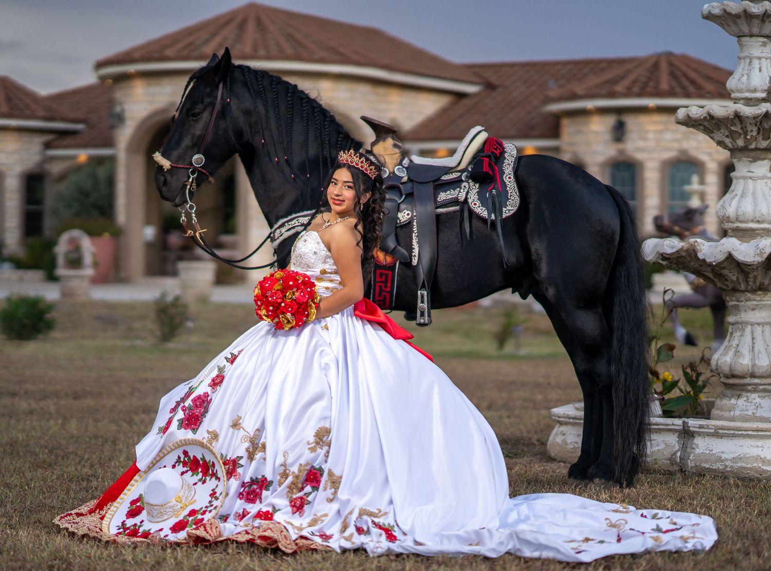 A flowing white gown with red embellishments trails on the ground beside a black horse.