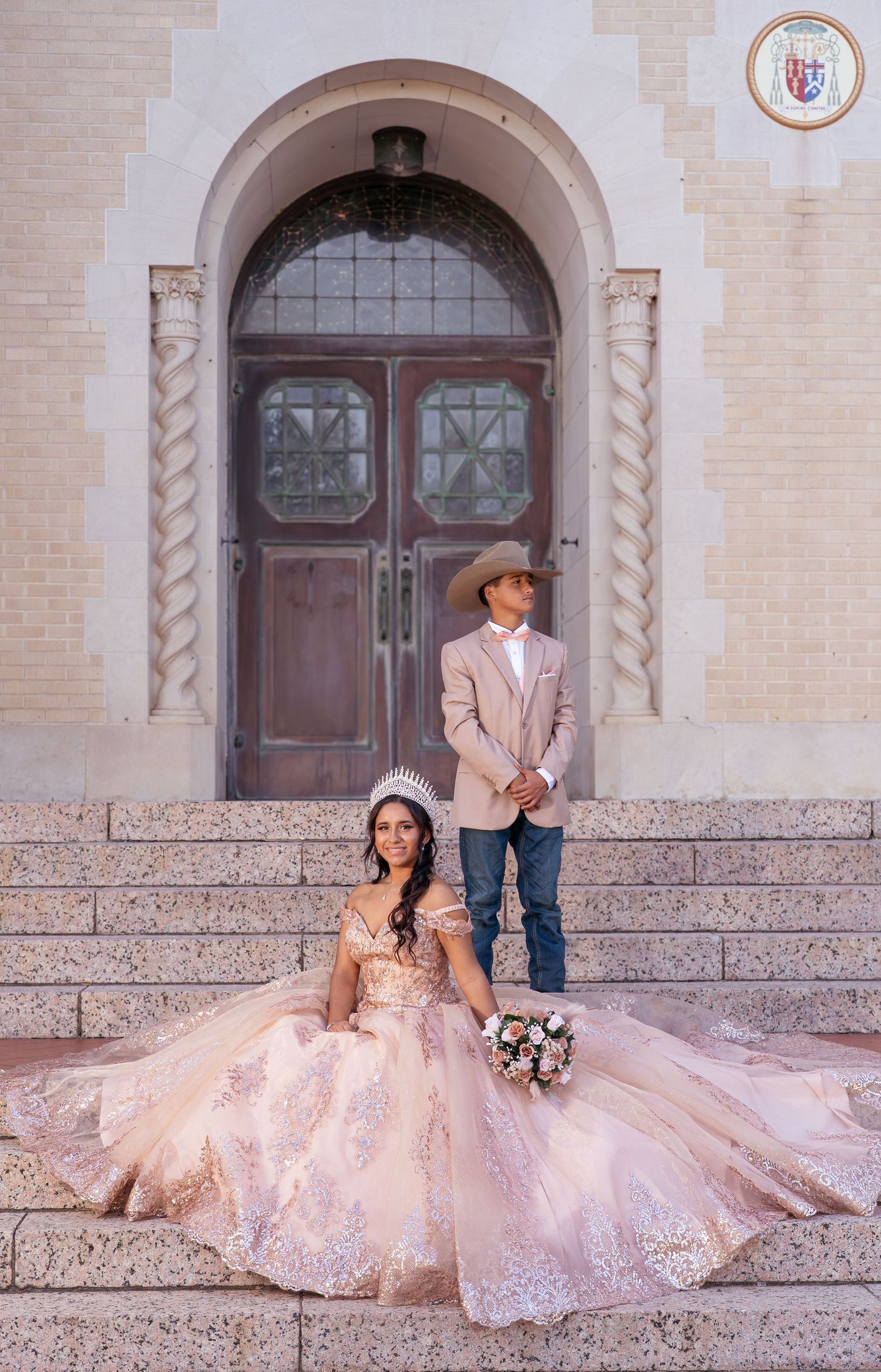 Romantic couple in formal attire sits on stone steps of historic building with ornate wooden doors.