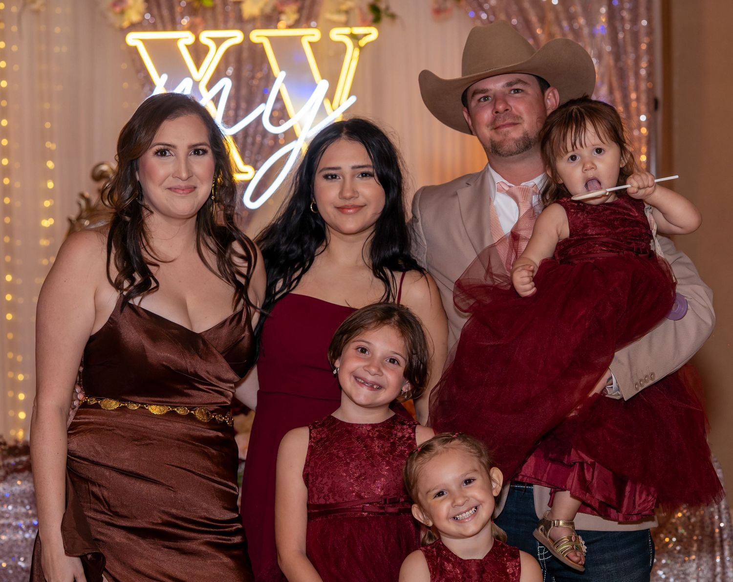 Family of five posing at a quinceañera party with illuminated XV sign in background.