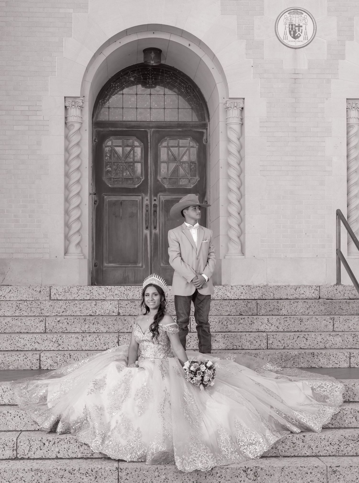 A black and white wedding photo of a couple posing on stone steps in front of an arched doorway entrance.
