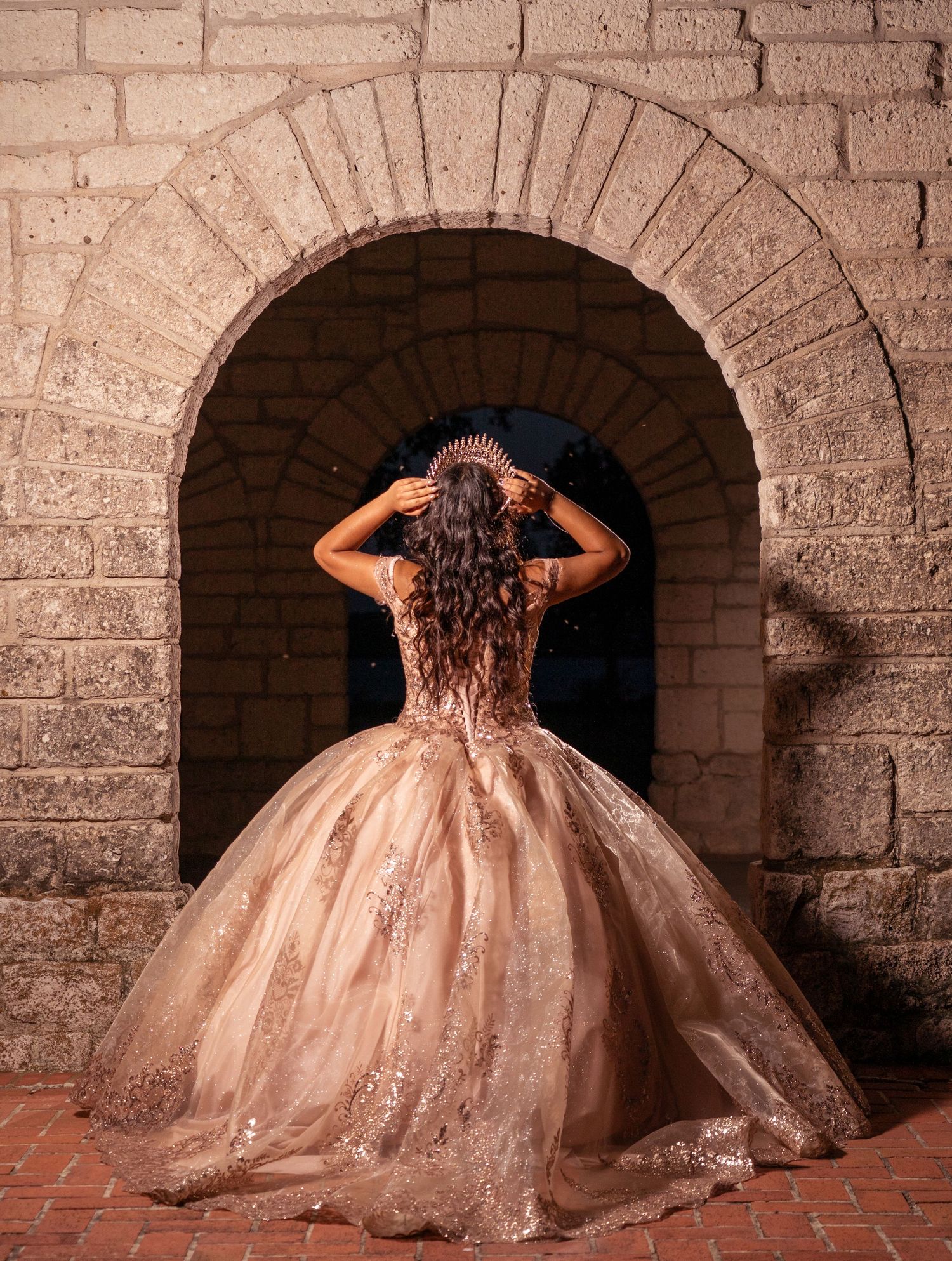 Back view of a rose gold ball gown with detailed beadwork framed by a stone archway.