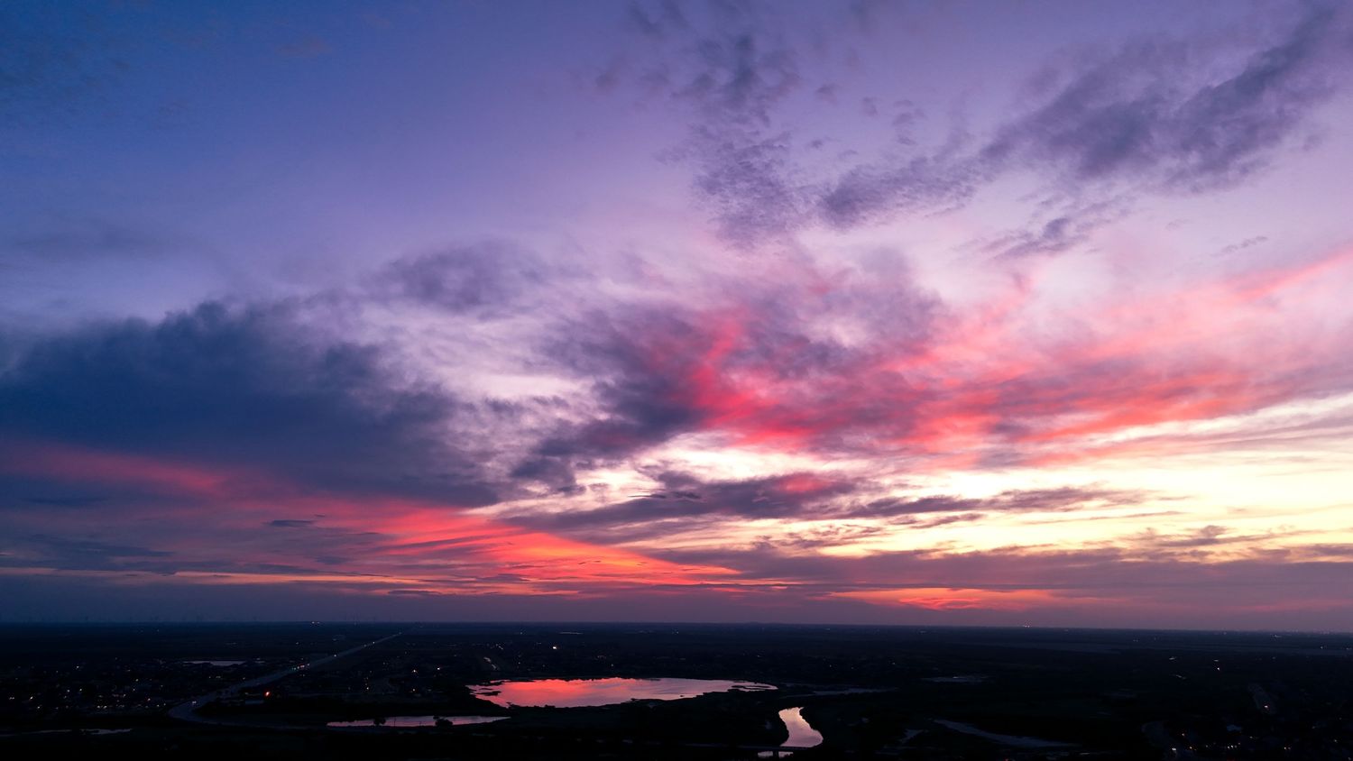 A dramatic purple and pink sunset sky over a dark landscape with a winding river reflecting the colorful clouds.