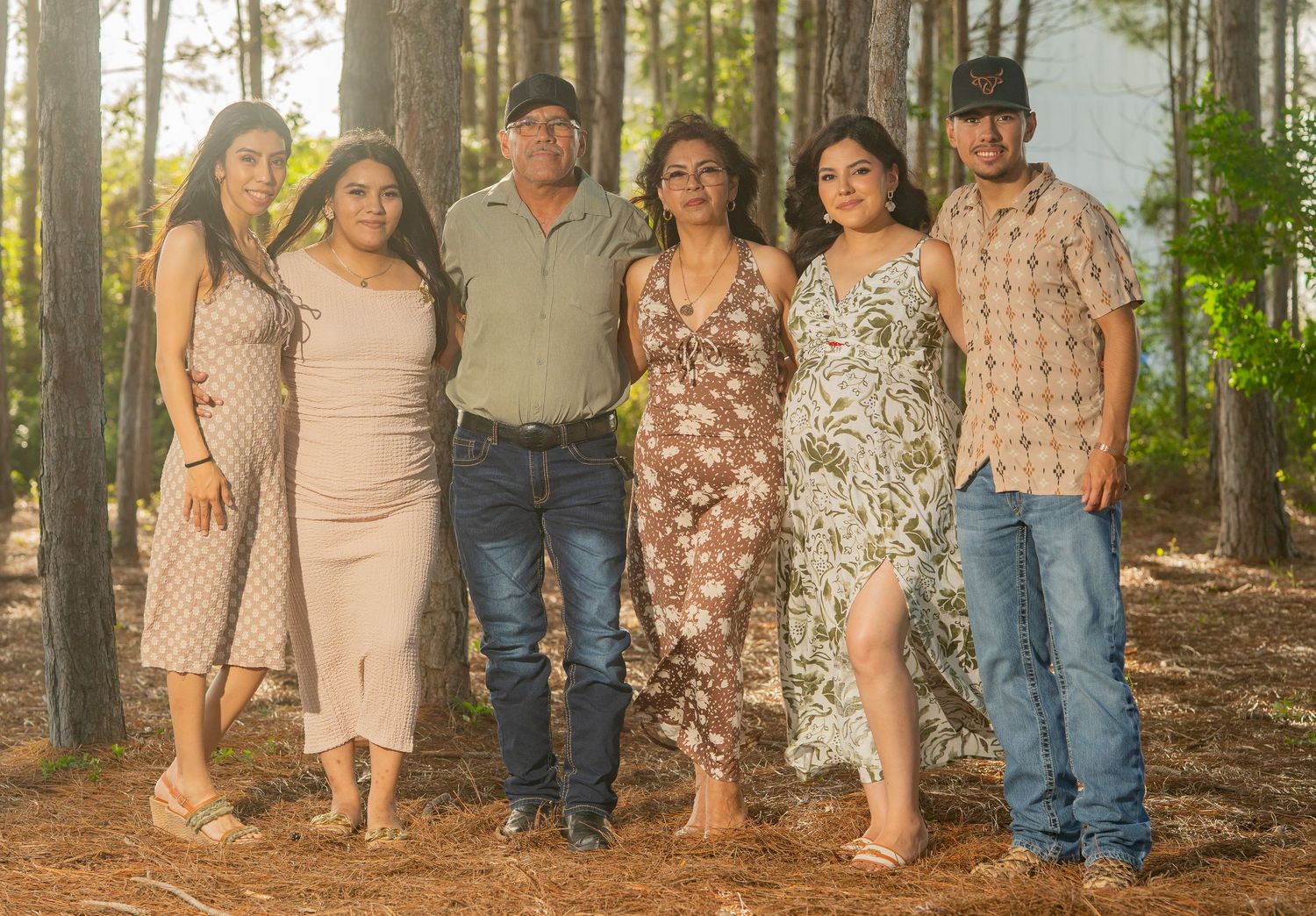 Family of six posing together outdoors among tall pine trees for a portrait photo session.
