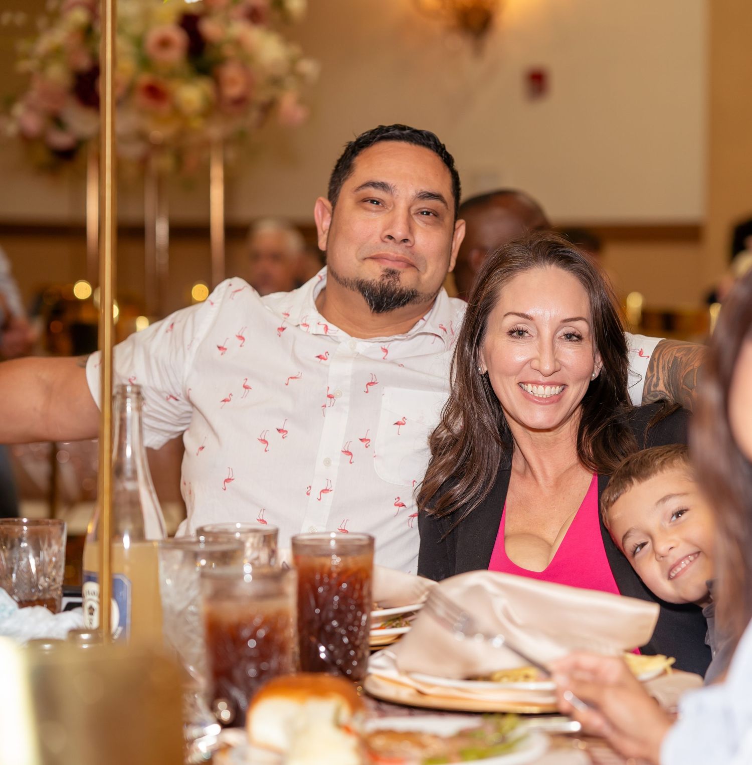 A smiling couple and young child pose together at a festive banquet table during a Quinceañera celebration.