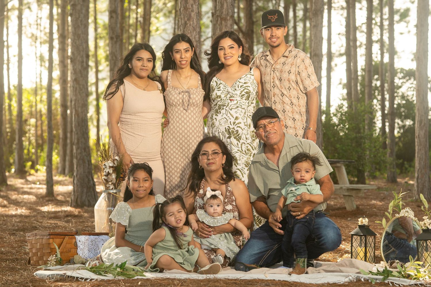 A multigenerational Hispanic family poses together outdoors in a pine forest for a professional portrait session.