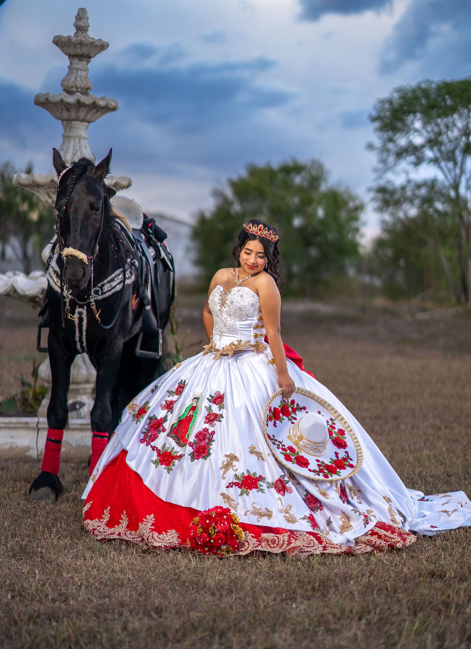 Dramatic quinceañera photos with black horse and white dress with red accents against cloudy sky.