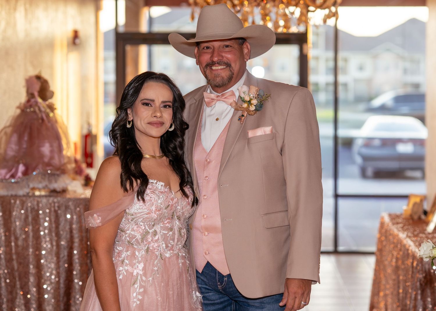 Couple dressed in formal attire posing at a quinceañera event with pink decorations.