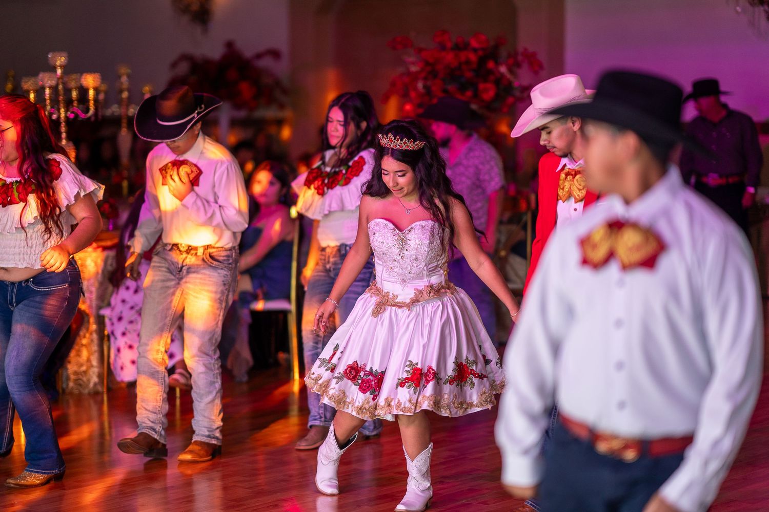 Wedding reception guests dance together on a dimly lit dance floor illuminated by vibrant purple and red lighting.