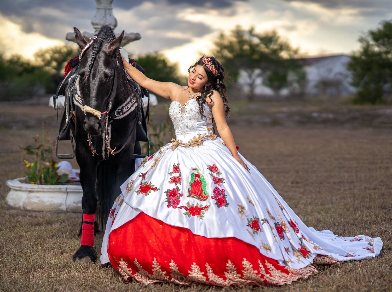 A white and red embroidered dress flows across the ground next to a black horse.