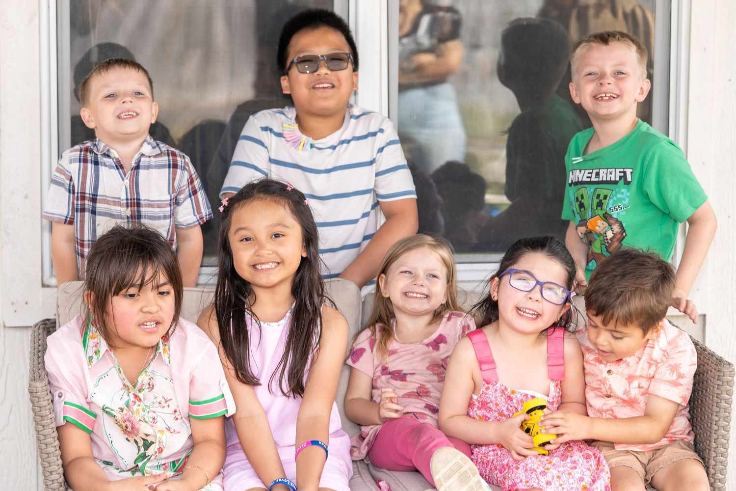 Group of seven young children smiling together on a porch for a family gathering photo.