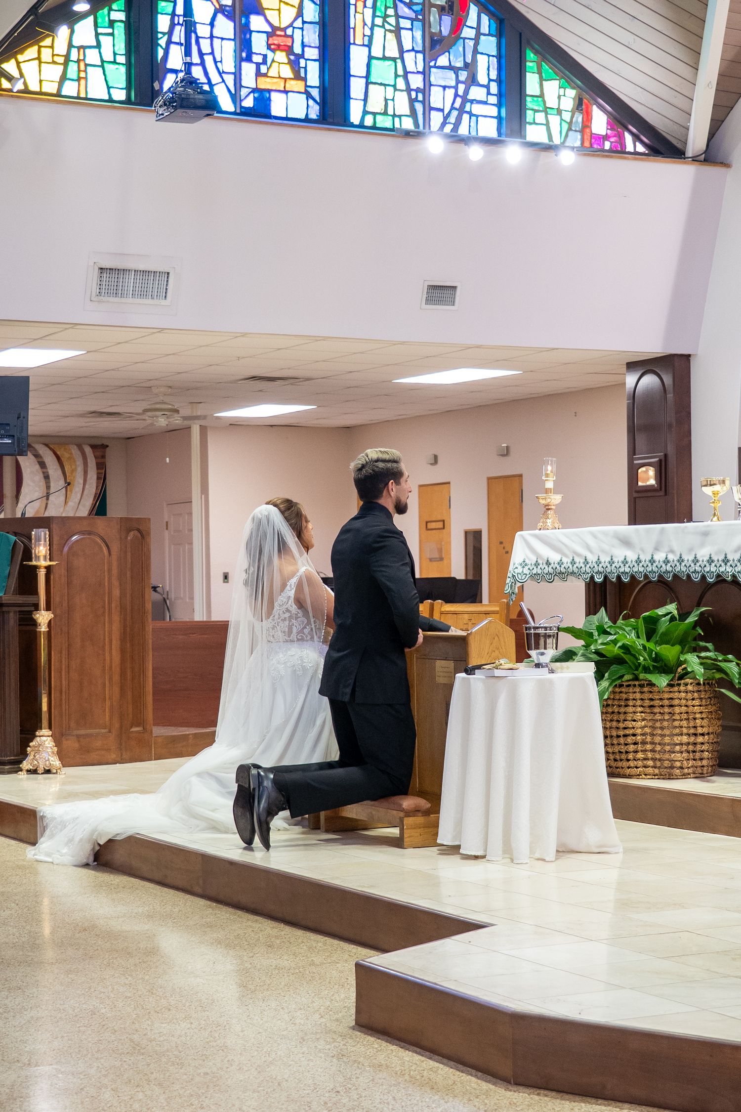 Bride and groom kneel at altar during Catholic wedding ceremony in church.