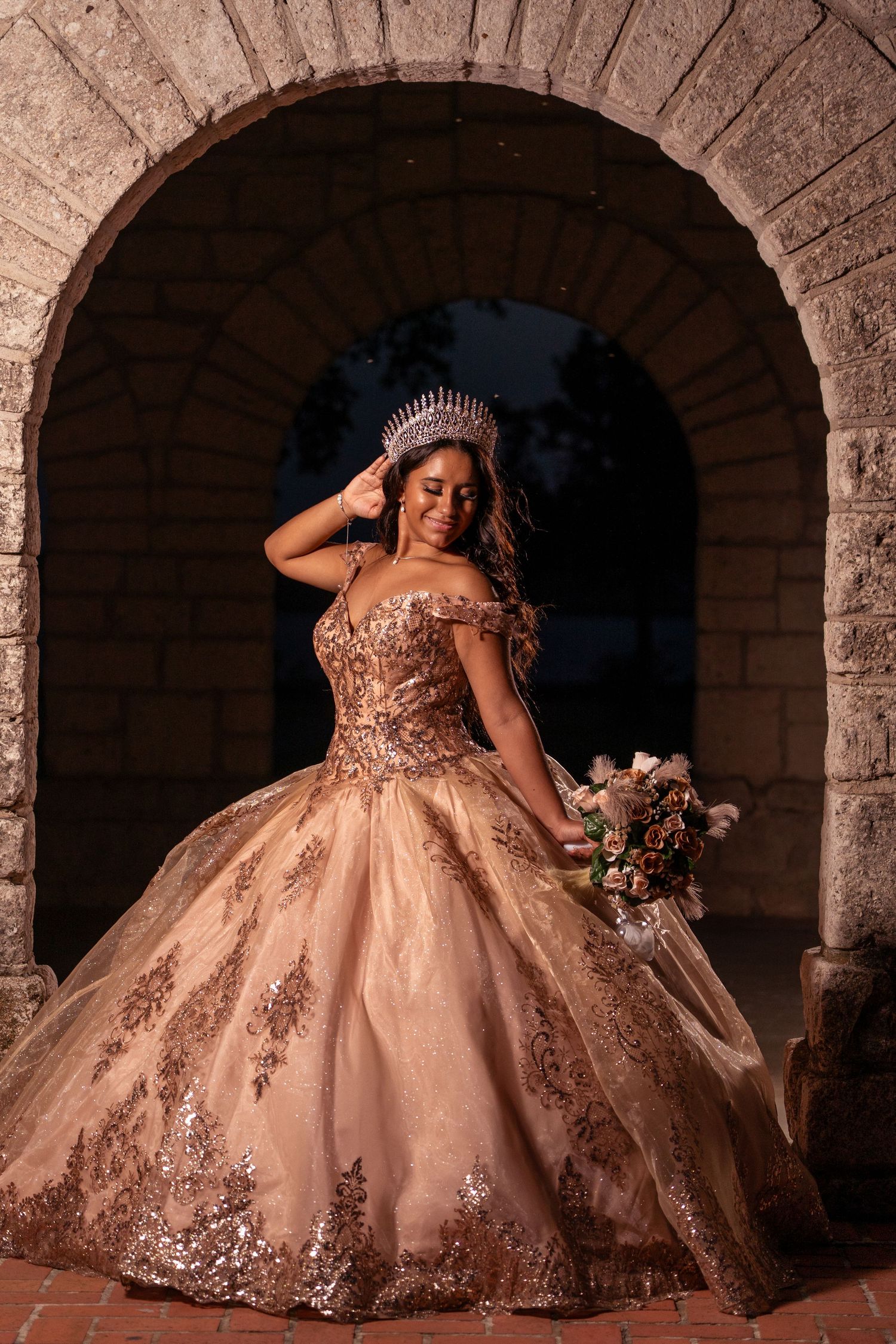 An elegant ball gown with beaded details is showcased under a stone archway during golden hour.