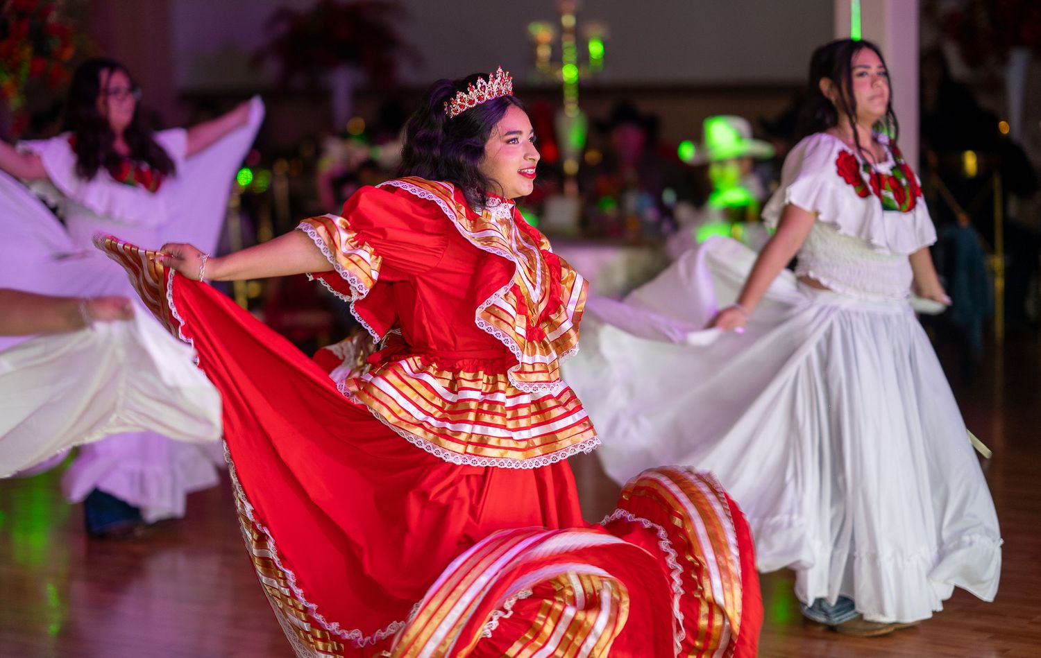 Dancers in flowing red and white traditional Mexican dresses perform a choreographed routine at a cultural celebration.