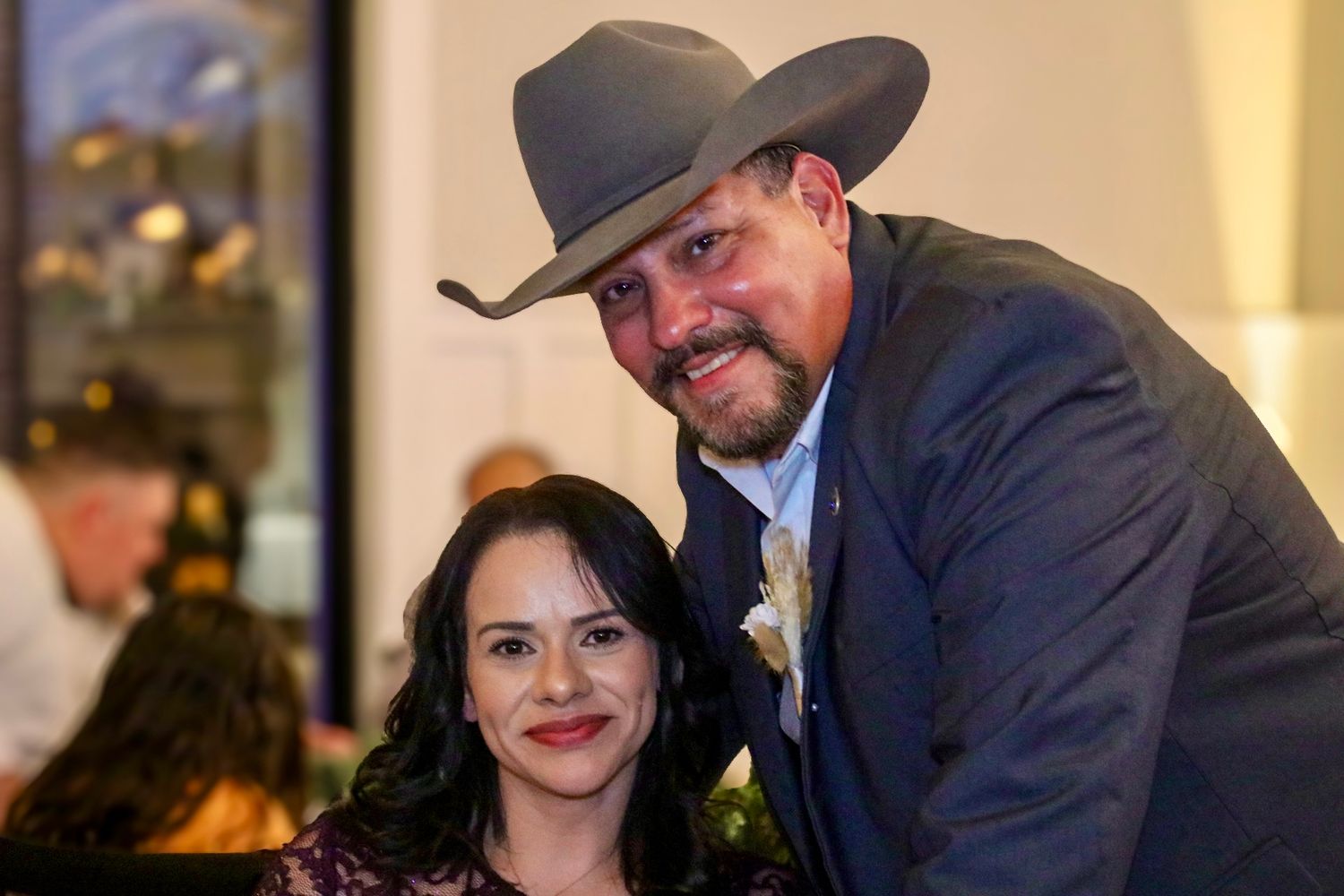 A couple poses at an indoor event, with one wearing a cowboy hat and suit.