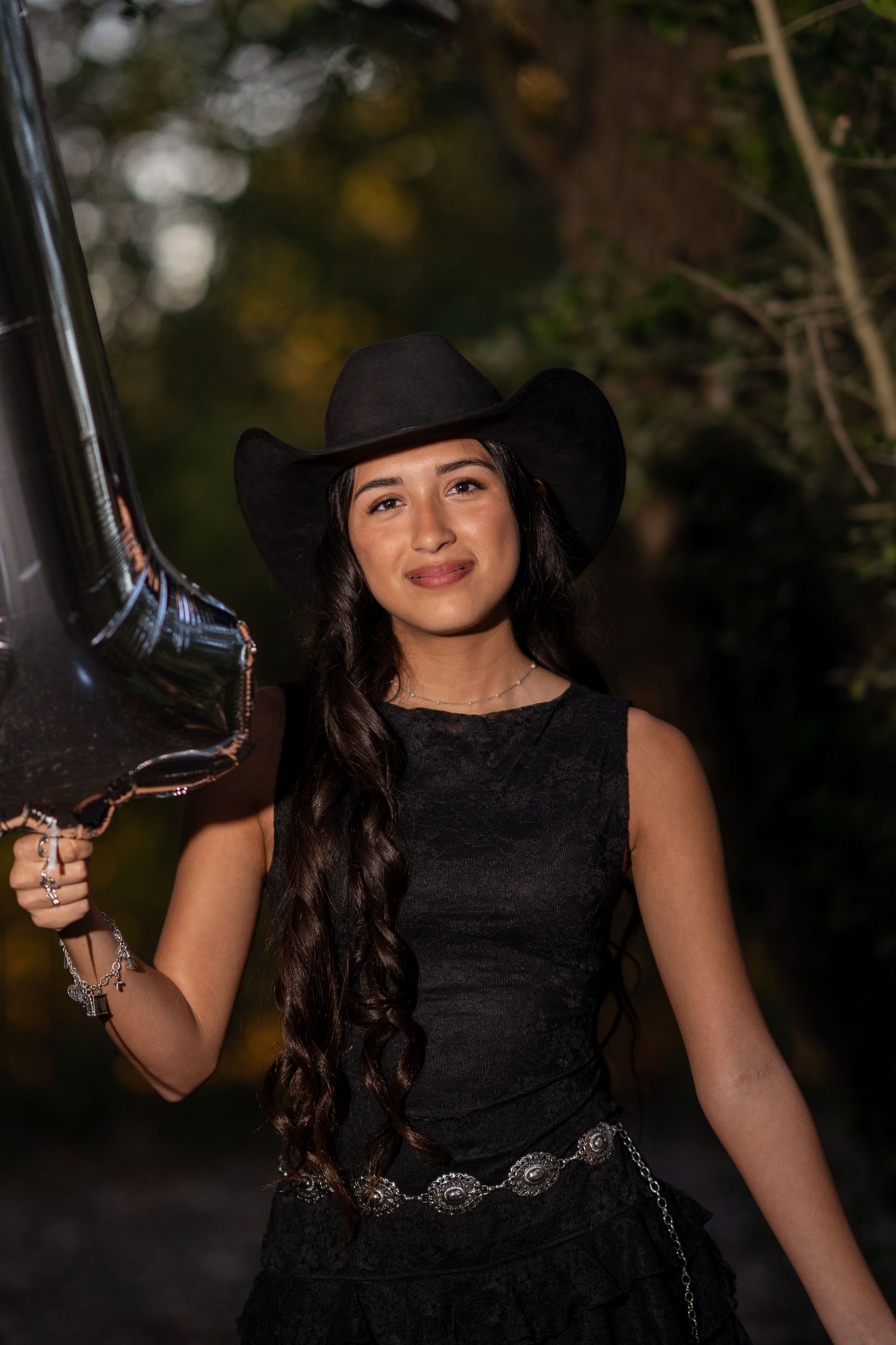 Young woman in black cowboy hat and lace dress holding a balloon, smiling outdoors.
