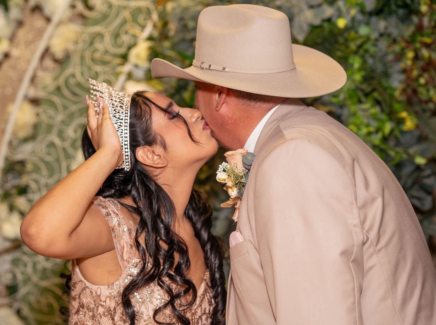 Couple shares a kiss at a wedding ceremony, groom in tan cowboy hat and suit.