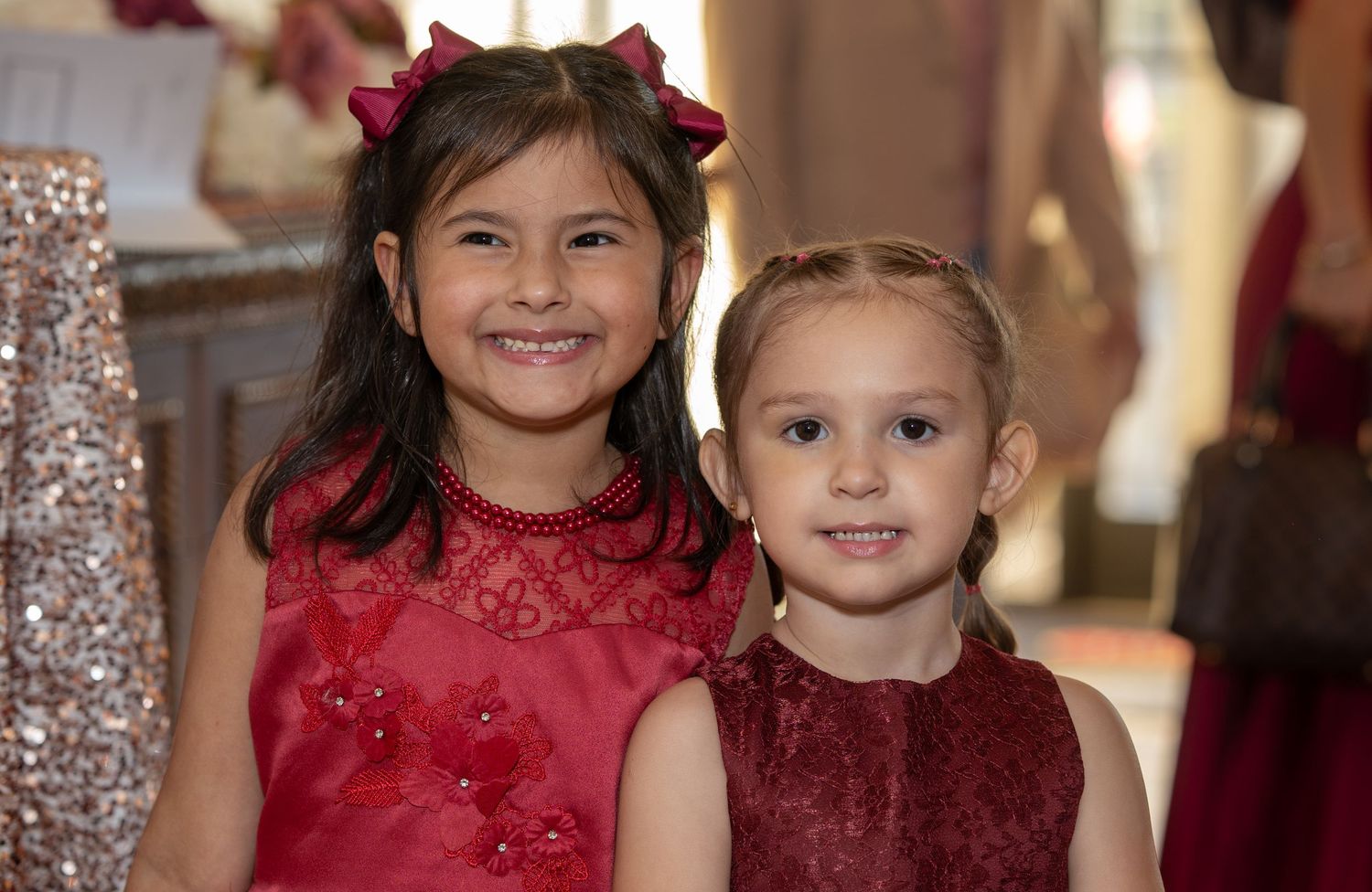 Two young girls in matching red dresses smiling together at a formal event.