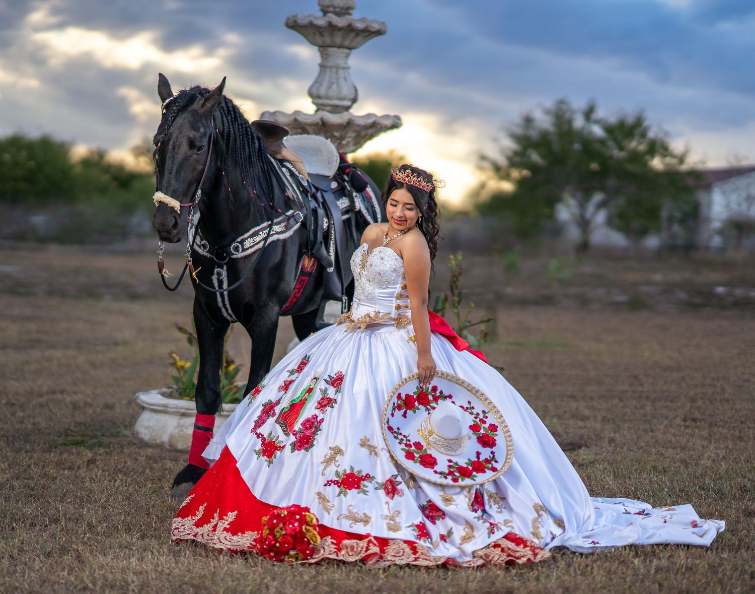 Dramatic portrait featuring a white and red embroidered gown beside a majestic black horse at dusk.