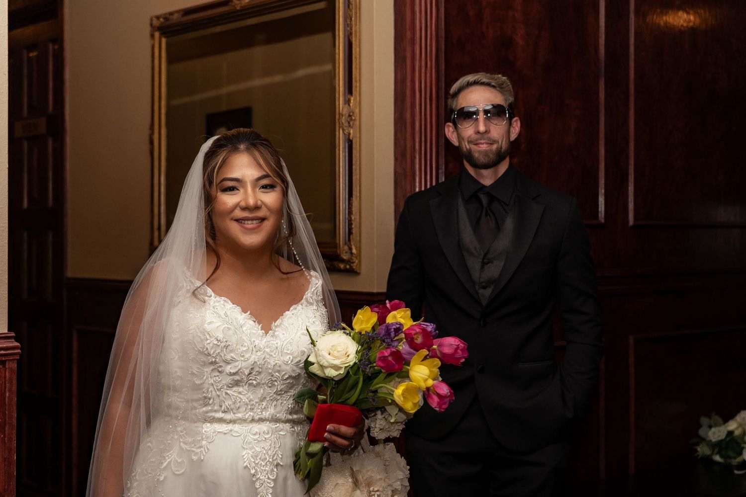 Wedding party members pose together in formal attire at an elegant indoor venue with warm lighting.