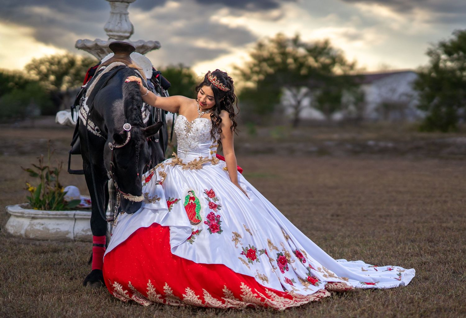 A white and red wedding dress with floral details is showcased against a dramatic sunset sky.