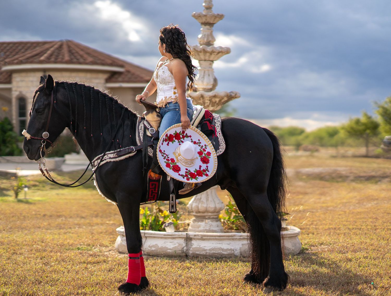 A stunning white and red quinceañera dress flows across the ground next to a black horse.