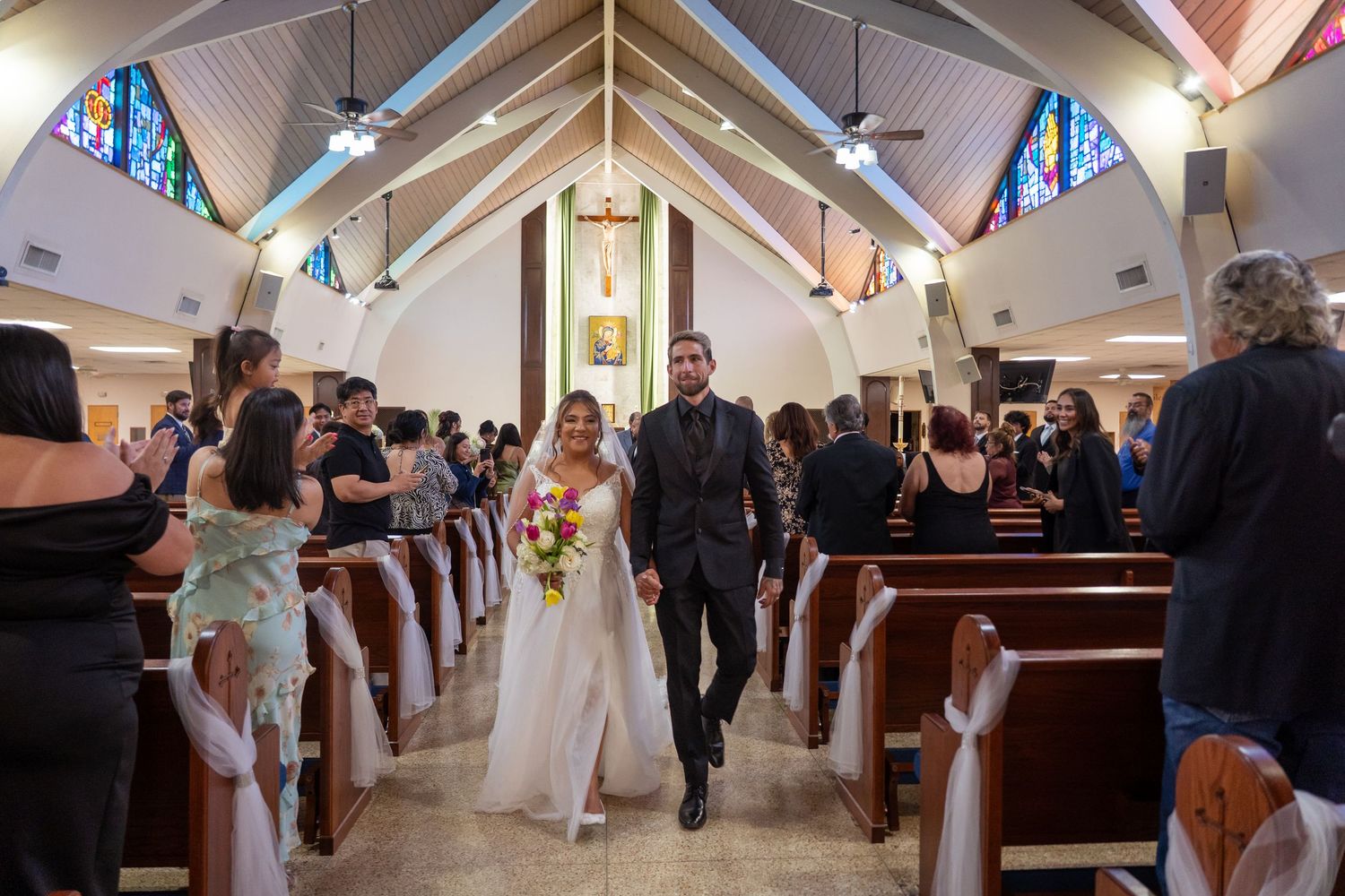 Newlyweds walk down church aisle after wedding ceremony with guests applauding.