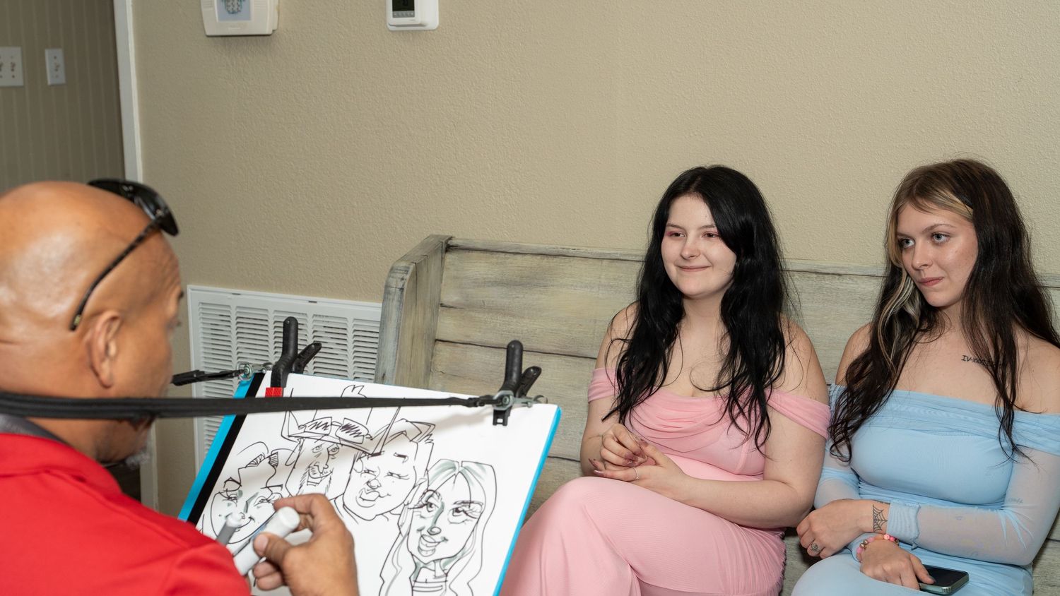 A caricature artist sketches two young women in formal dresses at what appears to be a special event or prom.