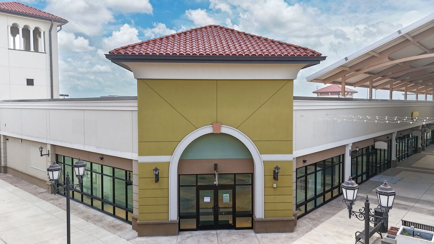 Modern yellow and white commercial building entrance with arched doorway and terra cotta tile roof at a shopping center.