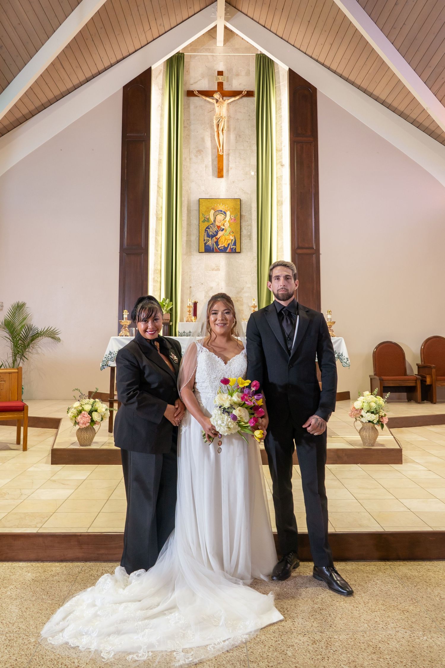 Wedding ceremony in a church with a crucifix and religious artwork displayed at the altar.