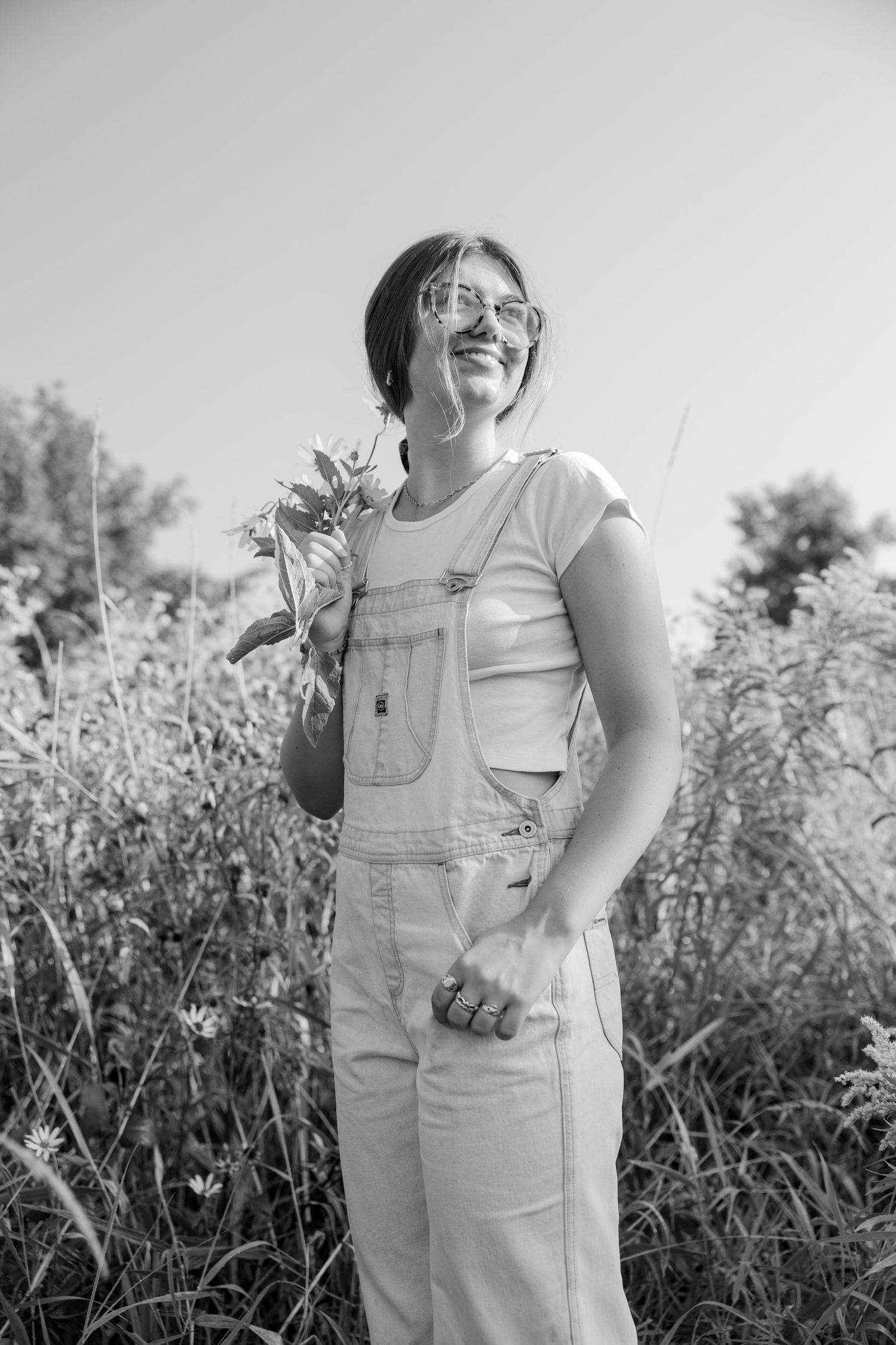 Joyful person in overalls and white t-shirt standing among wildflowers in black and white portrait.