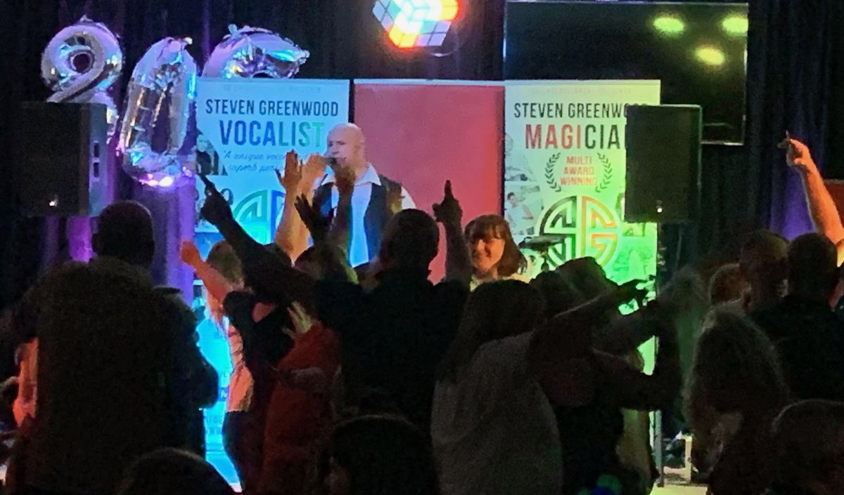 Energetic crowd dancing at a nightclub event with colorful stage lighting and banners.