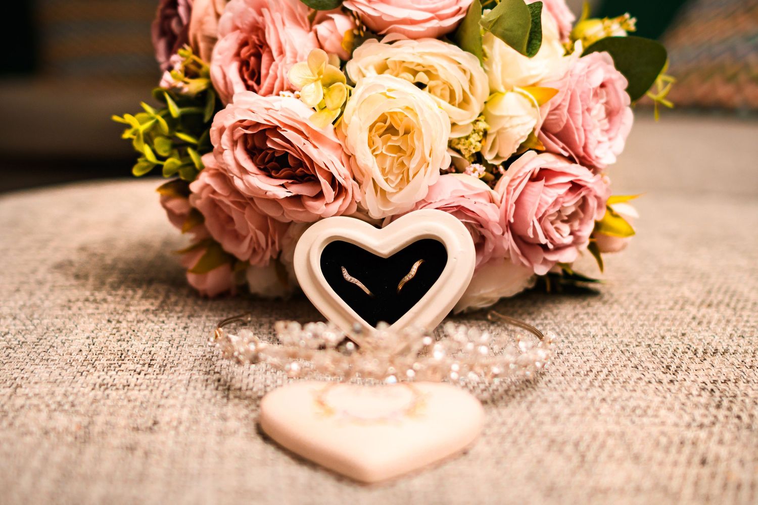 Heart-shaped ornament nestled among pink and cream roses on burlap texture.