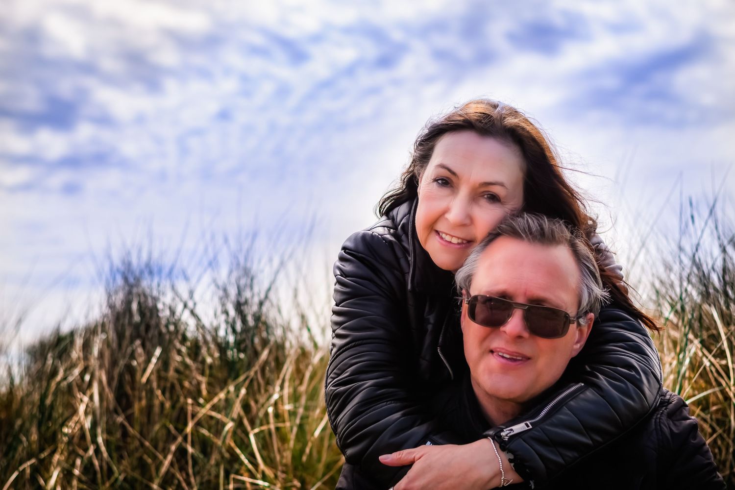 Happy couple sharing intimate moment together outdoors with blue sky and clouds.
