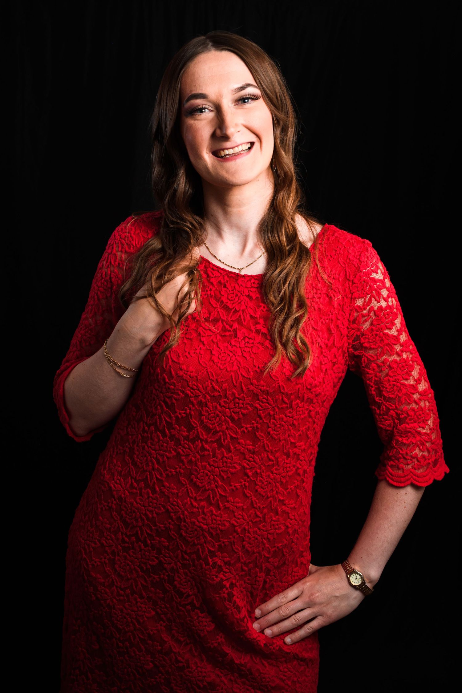 Portrait against black background wearing red lace dress and natural makeup.
