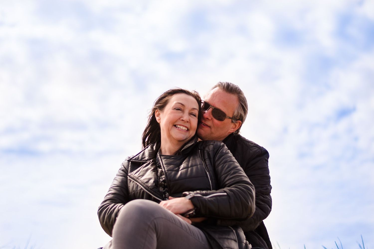 Couple embracing outdoors against cloudy blue sky background.