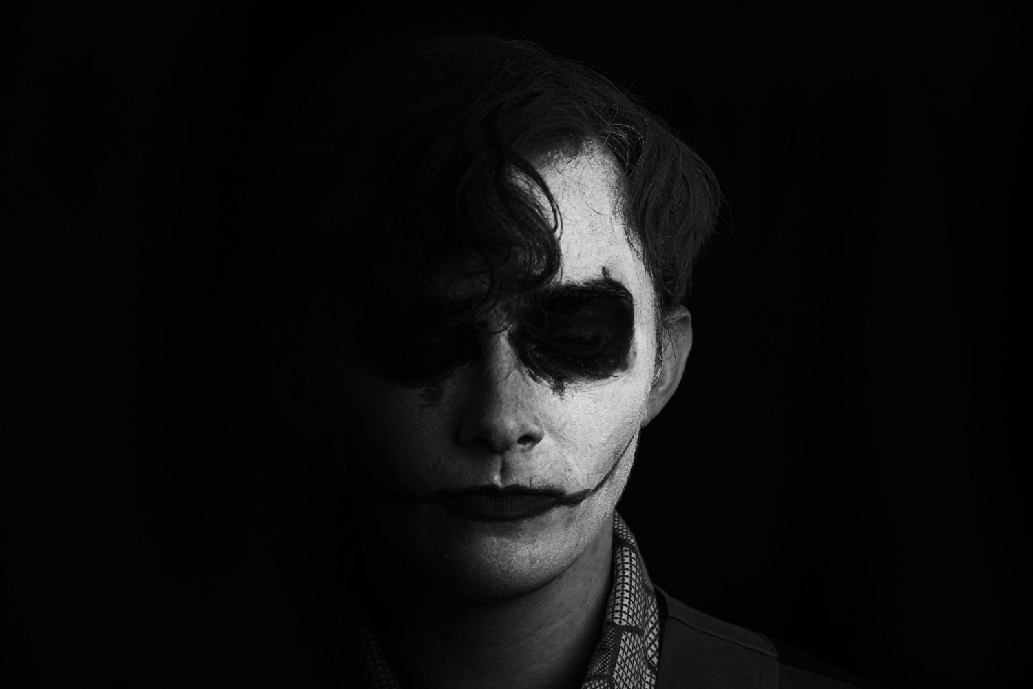 A haunting black and white portrait featuring dramatic face paint resembling a sinister clown or joker character.