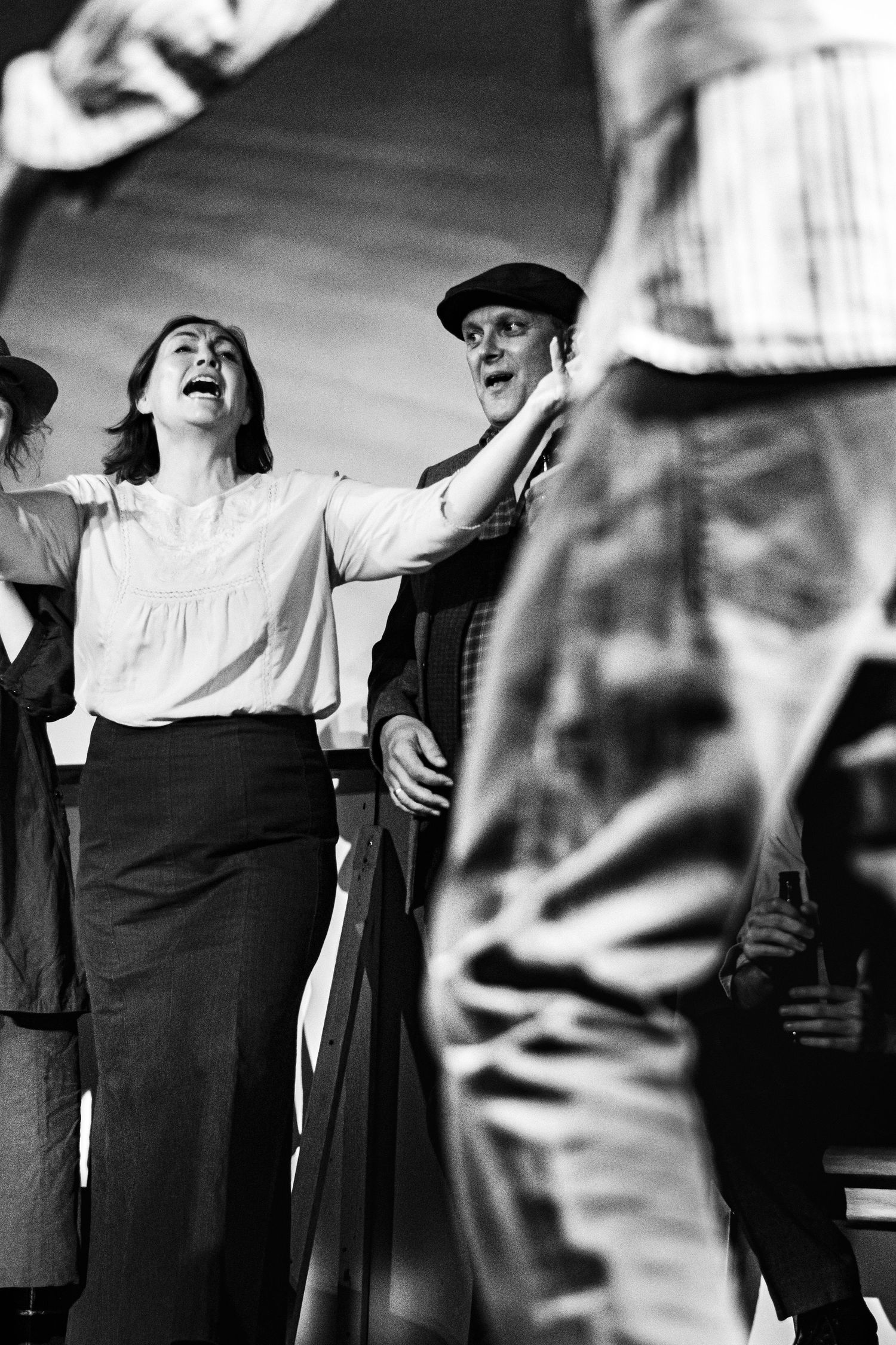 A dynamic black and white theater scene captures performers in vintage-style clothing during an energetic moment.
