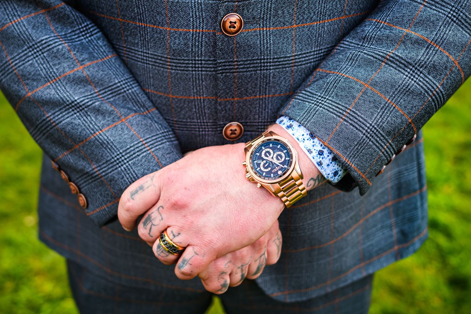 Close-up of groom's hands showing luxury watch and wedding ring with plaid suit sleeve.