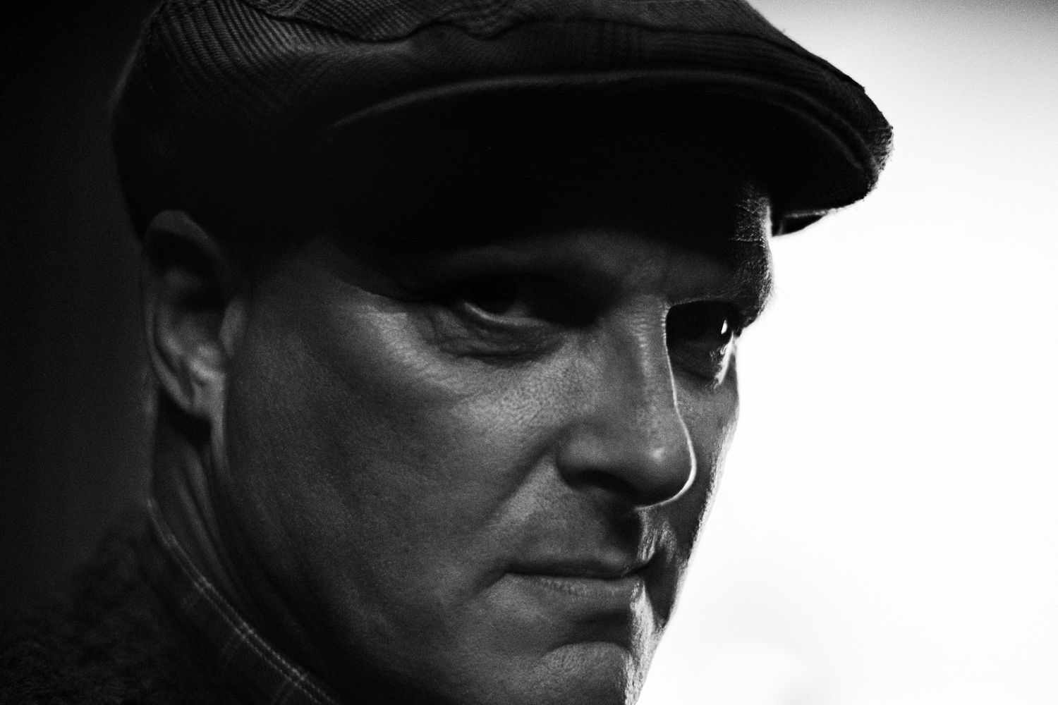 A dramatic black and white portrait of a person wearing a flat cap in shadows.
