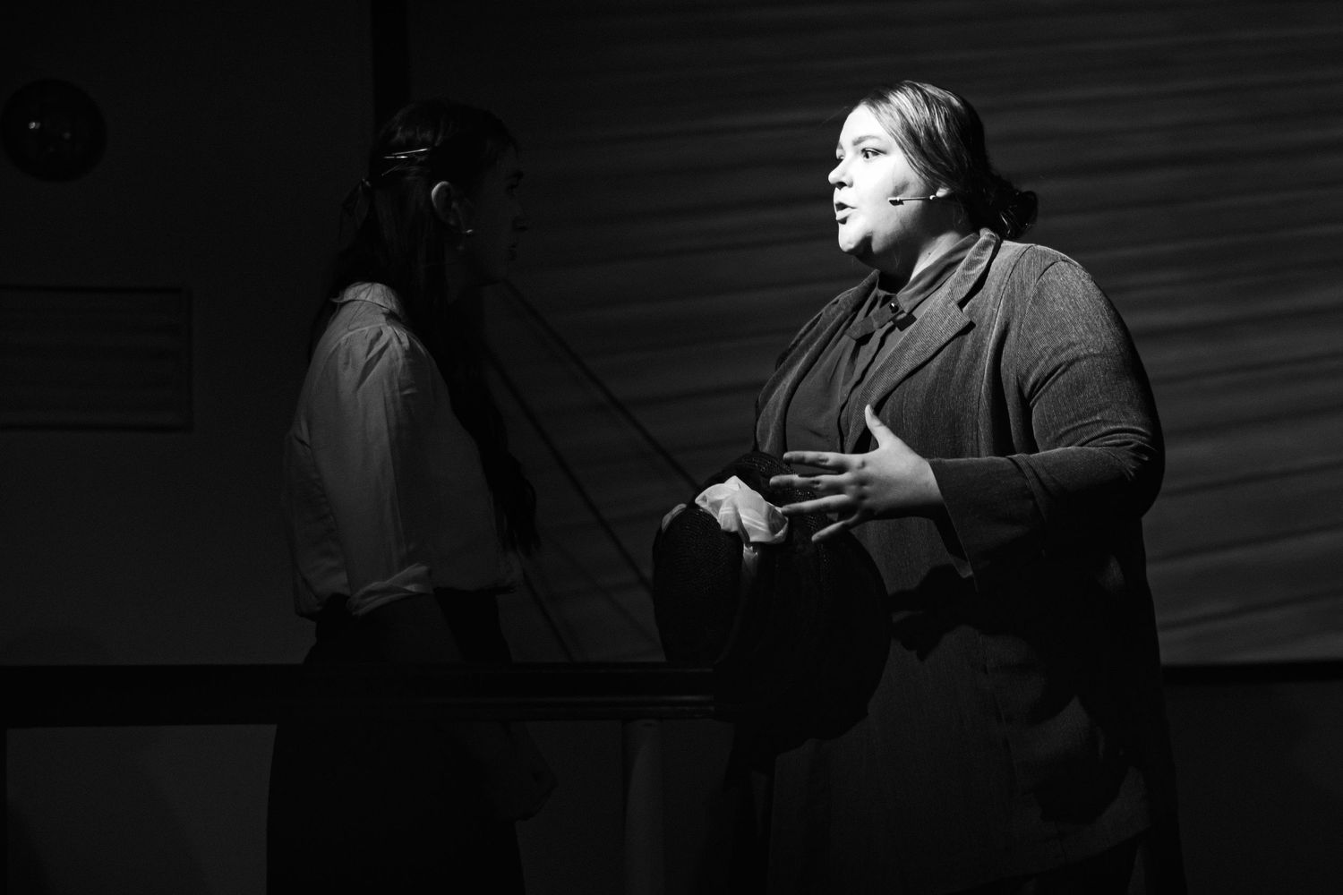 A dramatic black and white stage performance shows an expressive theatrical moment.