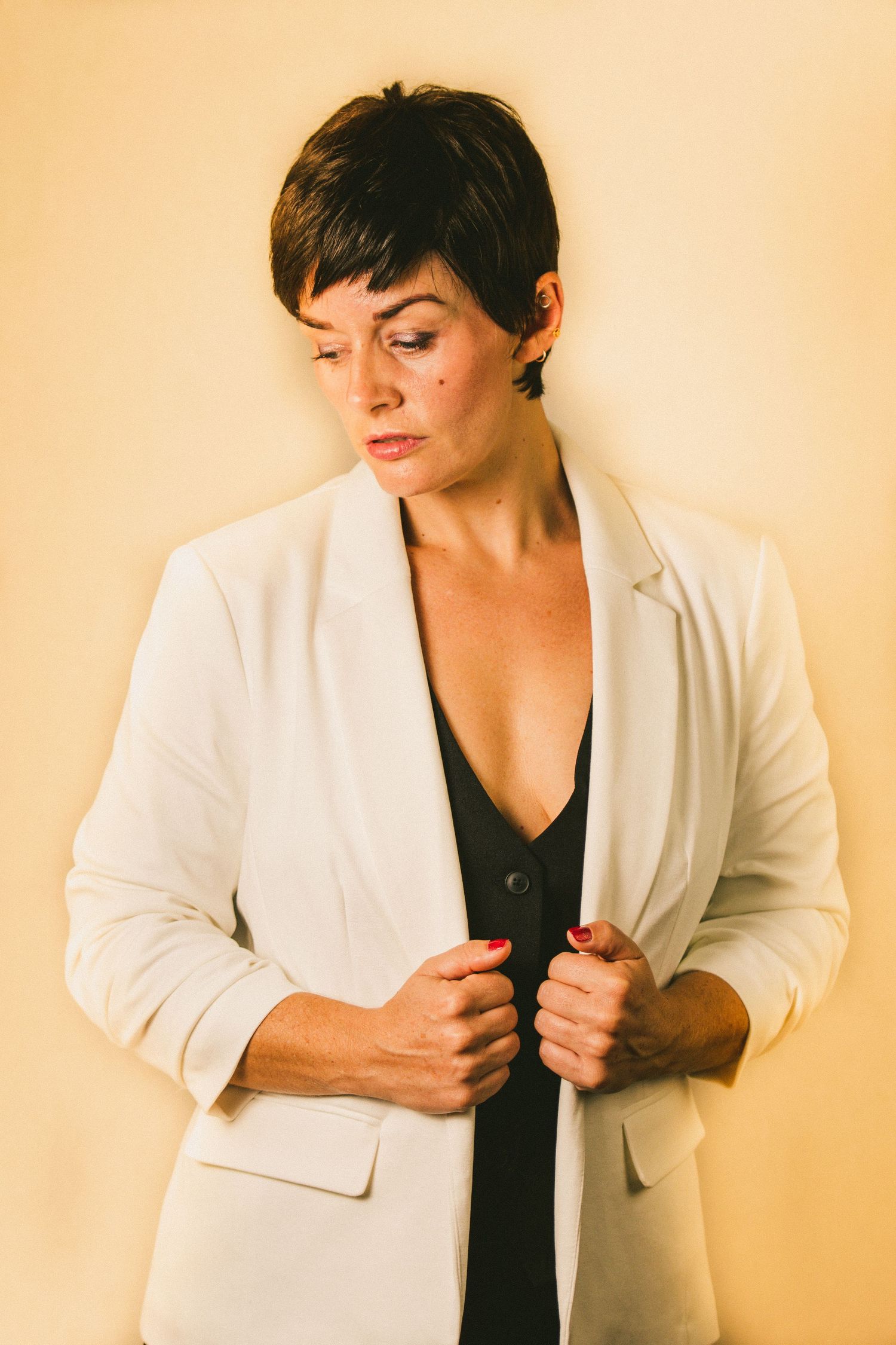 Fashion portrait of someone wearing a white blazer over black top against beige background.