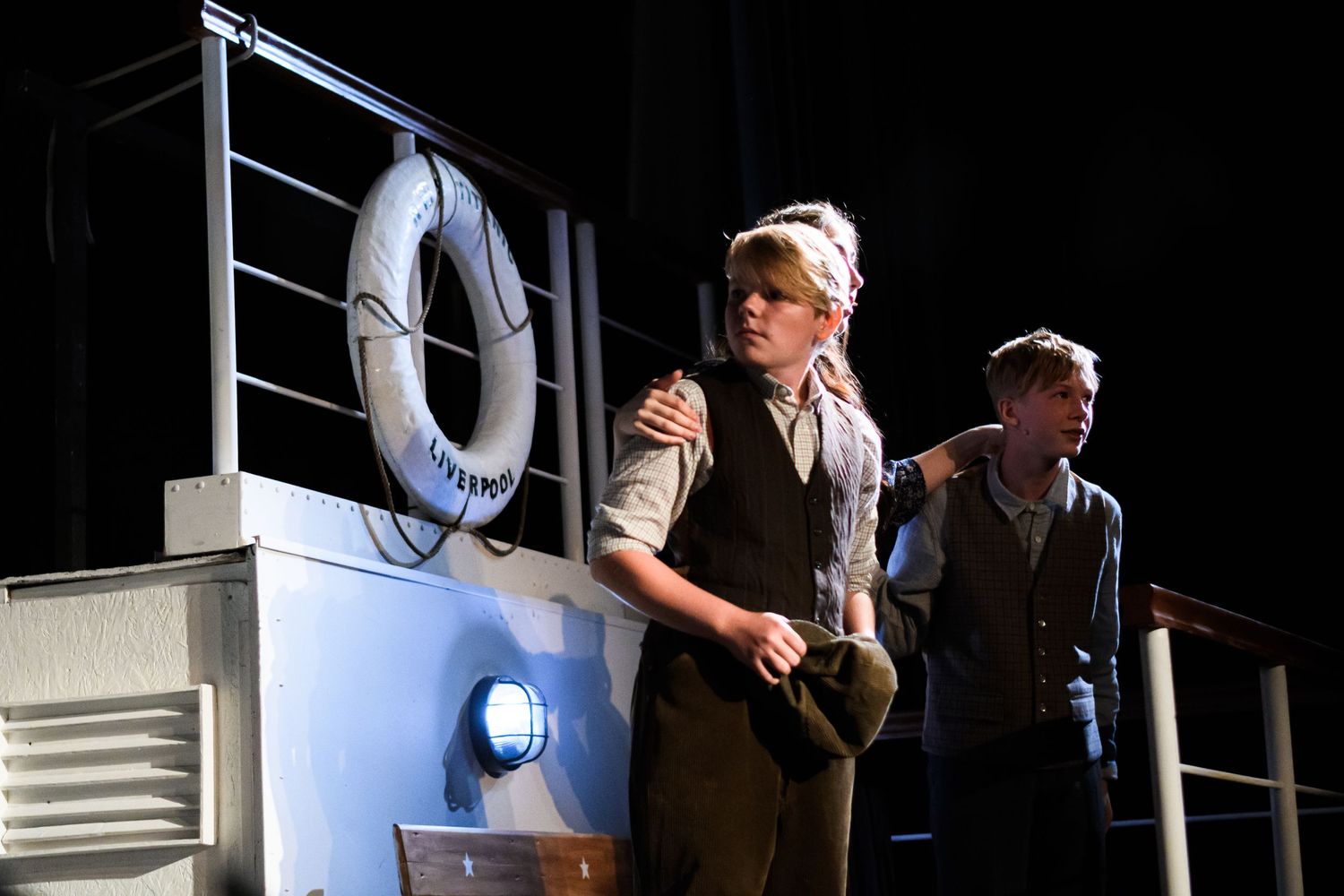 Two actors perform on a ship-themed stage set with a life preserver ring visible.