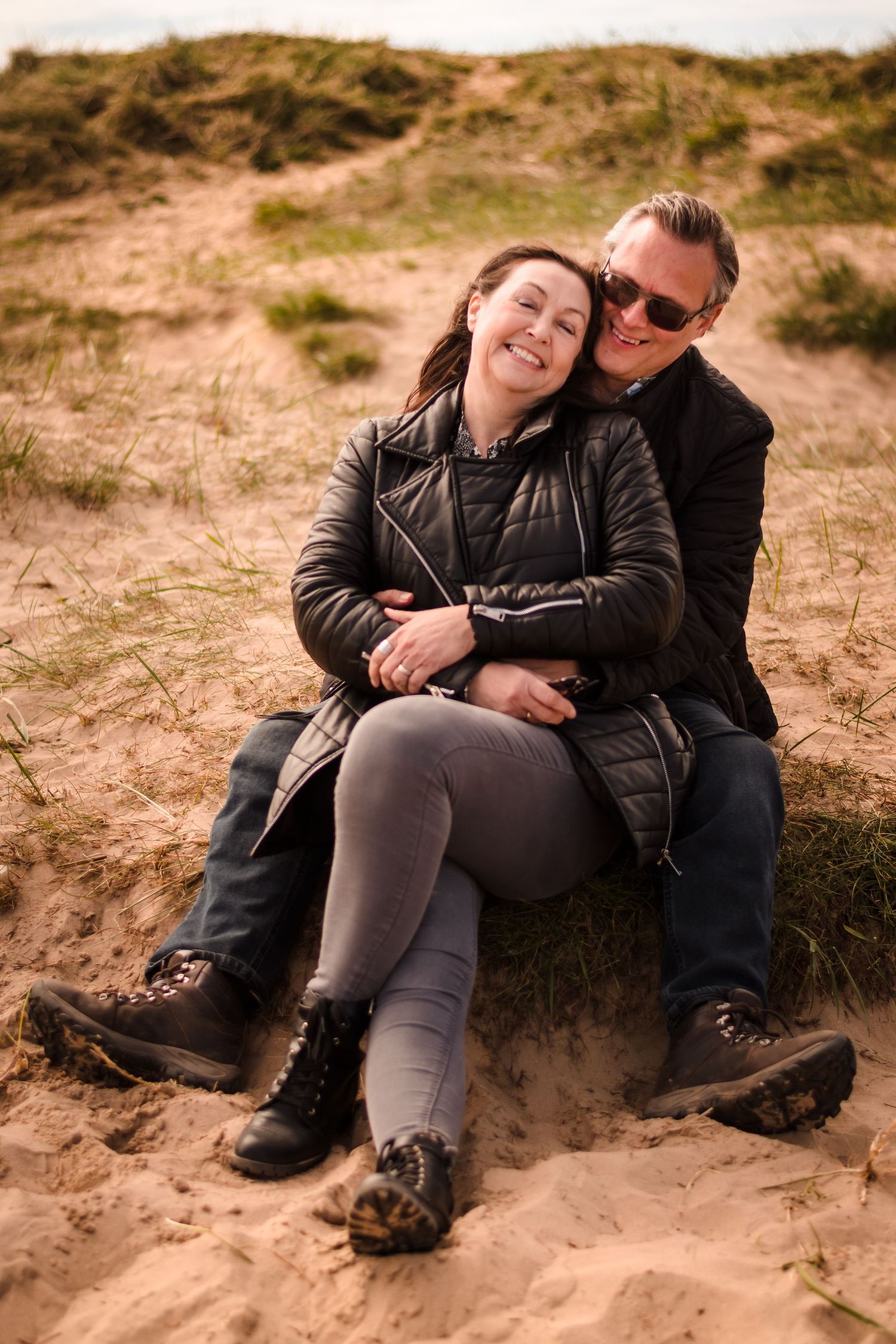 Couple sitting together on sandy dunes sharing a relaxed moment.