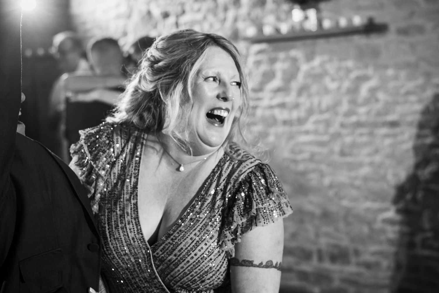 Woman in sparkly dress laughing joyfully while dancing at an event with stone walls in background.