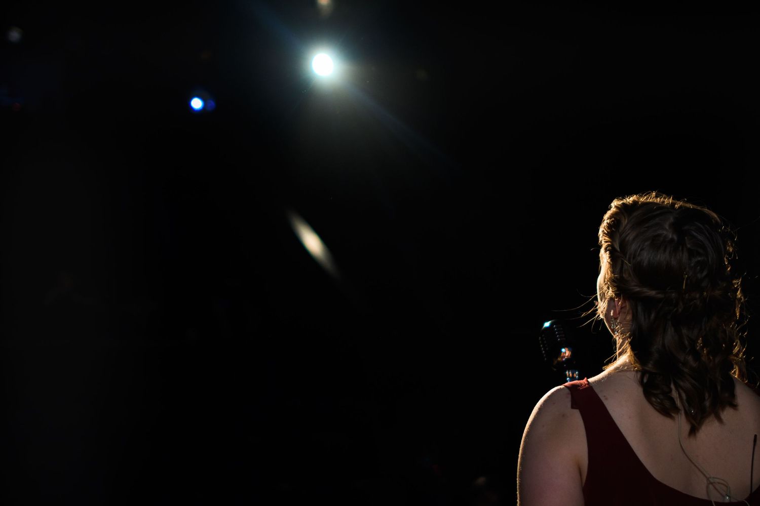Dramatic side view of performer on dark stage with bright spotlights creating atmospheric lighting effect.