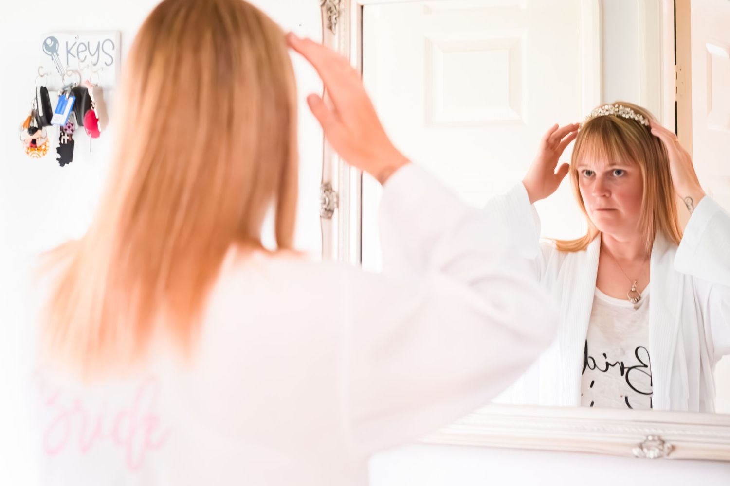 Person in white robe looking frustrated while styling hair in bathroom mirror.