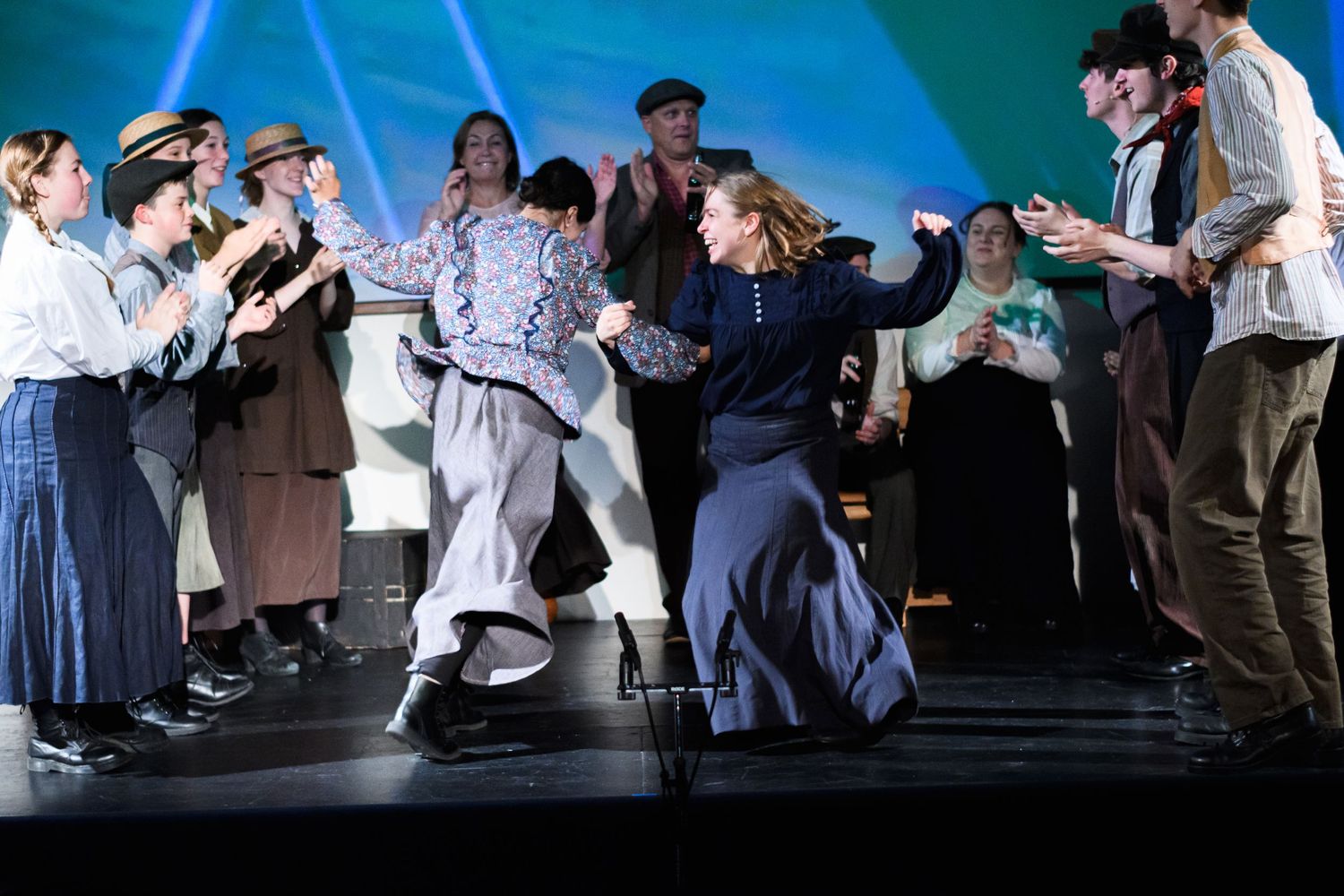 Theater performers engage in a lively dance scene on stage with dramatic blue lighting.