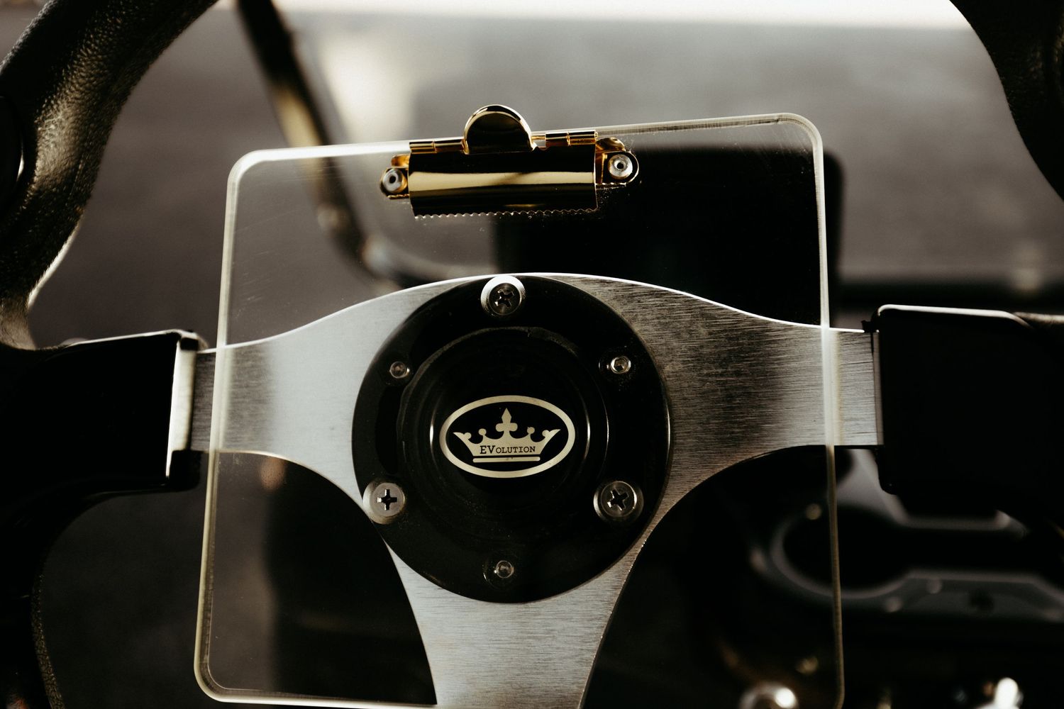 Close-up shot of a brushed silver steering wheel with a black crown logo emblem in the center.