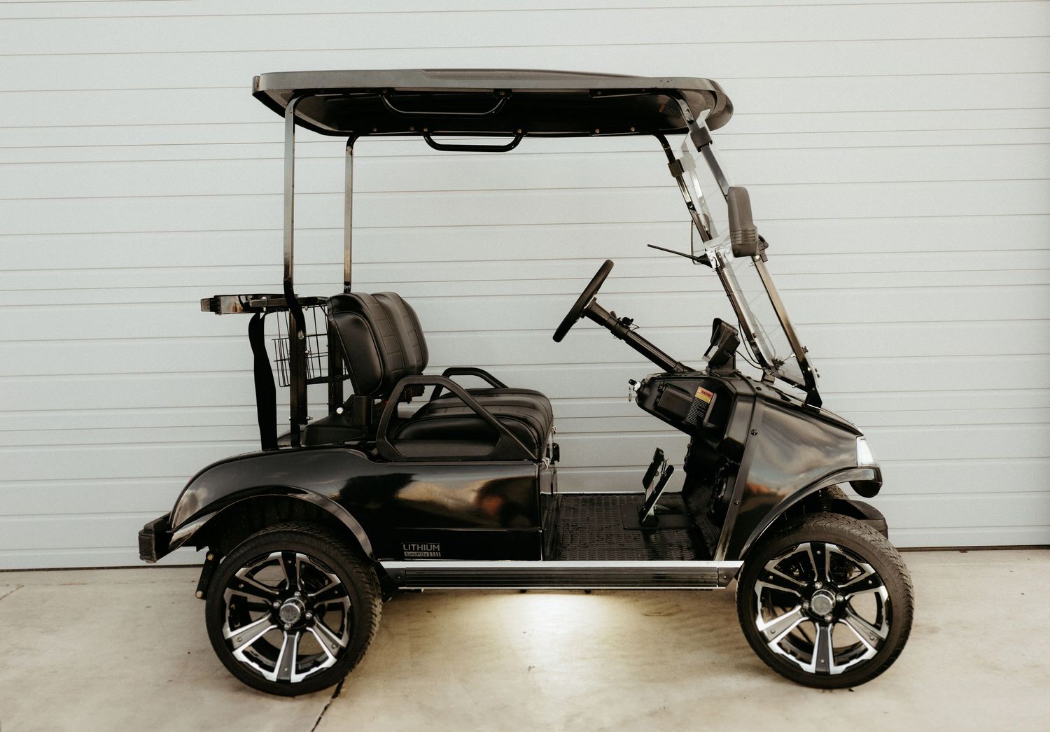 Custom black golf cart with chrome wheels and lifted suspension parked in front of white garage door.