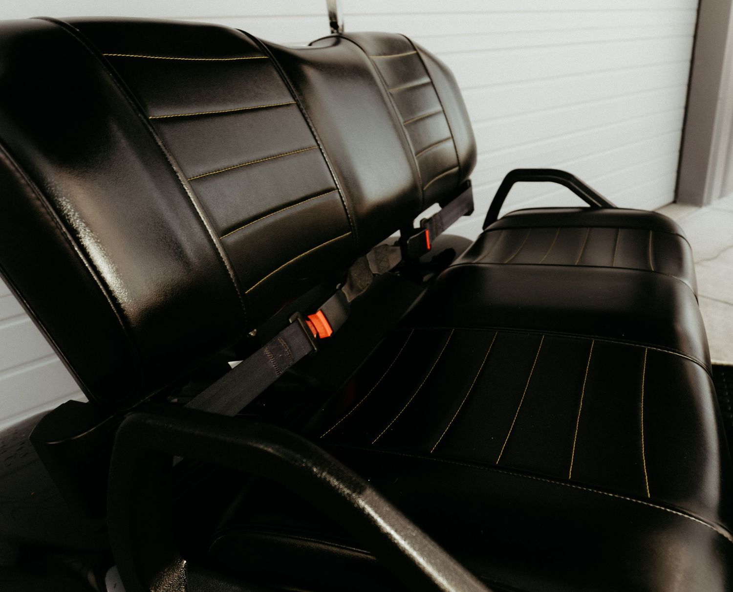Black leather car seats with vertical ribbed pattern and visible seat belt buckles in a dark interior.